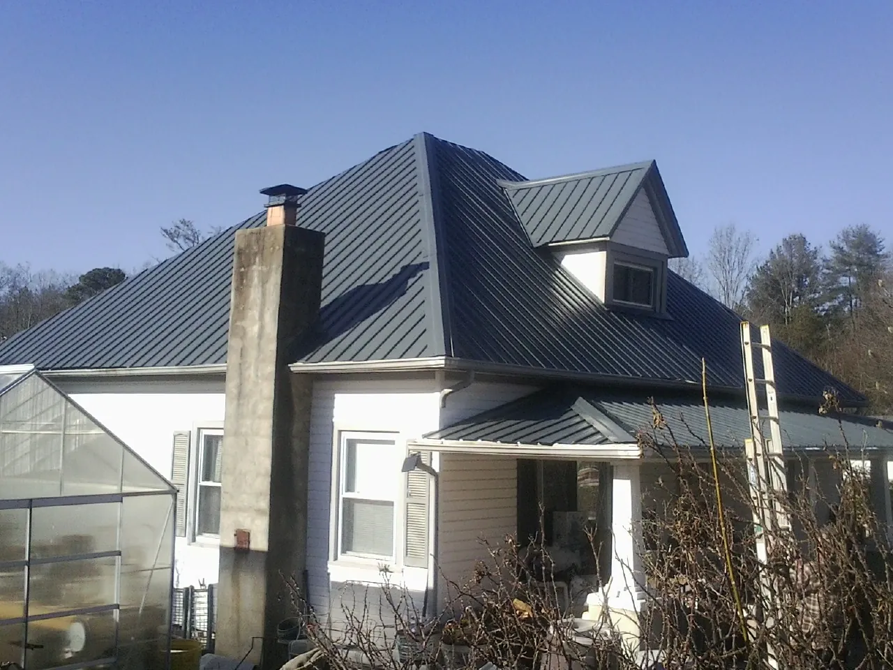 Dark blue standing seam metal roof on a white farmhouse with dormer — Slate & Tile Roof Repair by Roofing Brothers in Fall River