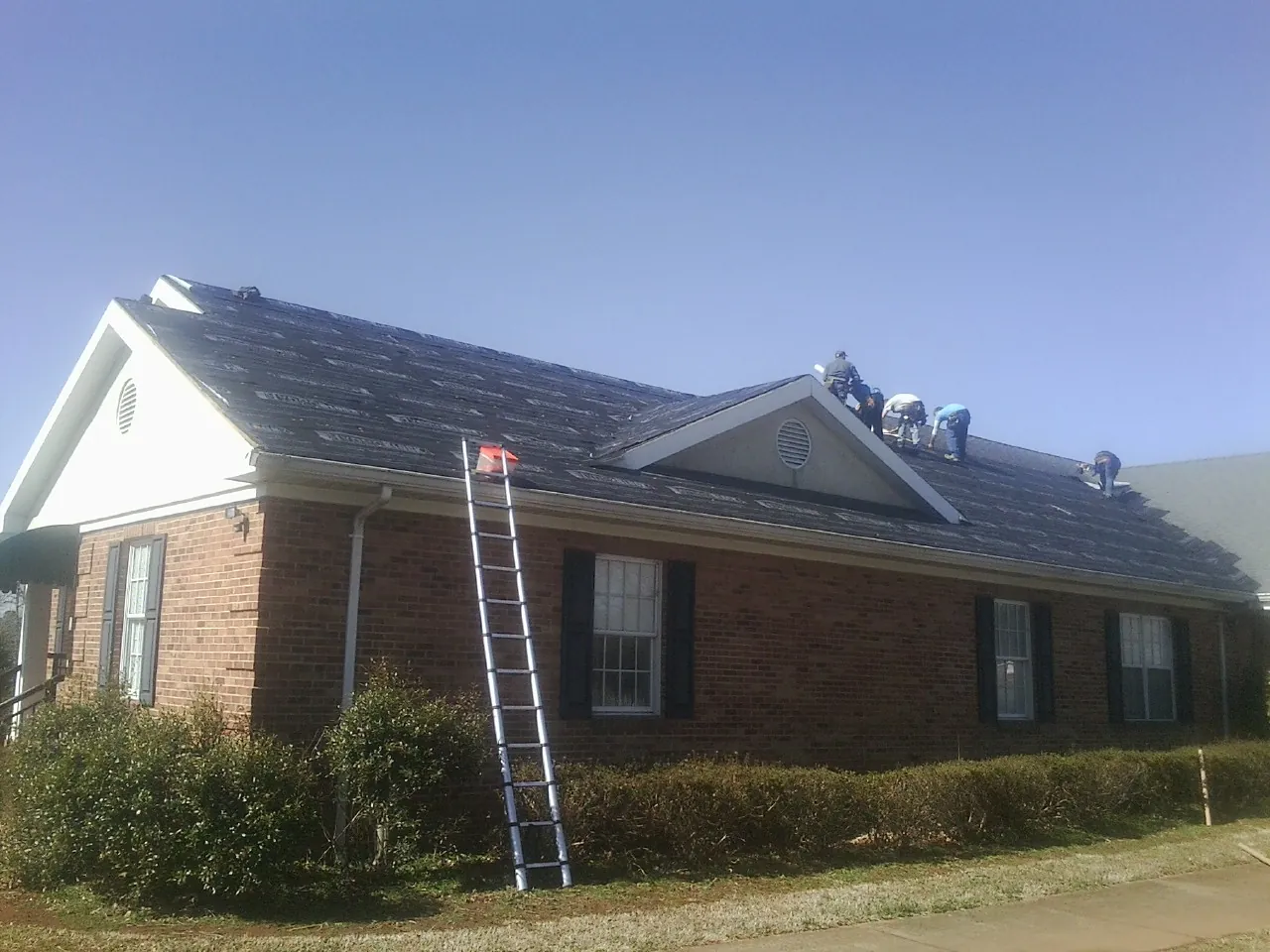 Crew tearing shingles off a brick ranch roof with a ladder set — Metal Roof Repair work by our crew in Fall River