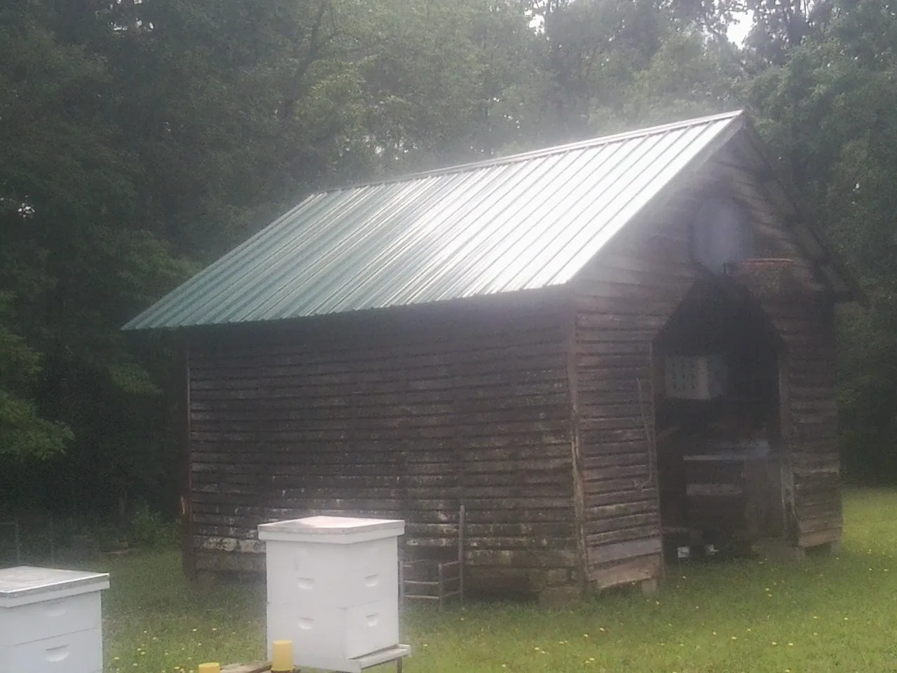 Green metal roof on a weathered barn beside stacked beehives in Fall River